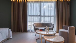 Habitación de hotel con cama, una mesa redonda, un sofá y vistas a la ciudad a través de amplias ventanas.