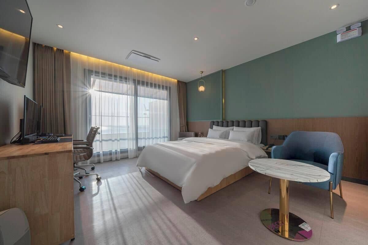 A hotel room with a bed, a desk, a chair, and a small table.