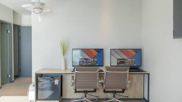 A modern office space with two desks, chairs, a small plant, and a wall-mounted TV displaying game titles.