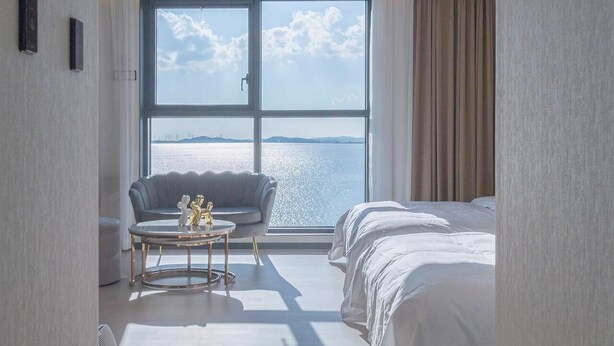 Una habitación de hotel con un ventanal grande, un sofá, una mesa de centro redonda y una cama.