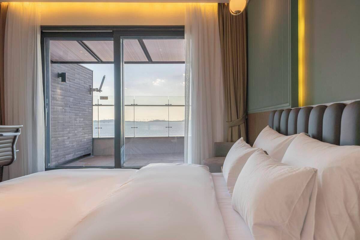 A hotel room with a large bed, a view through a glass door, and a modern design.