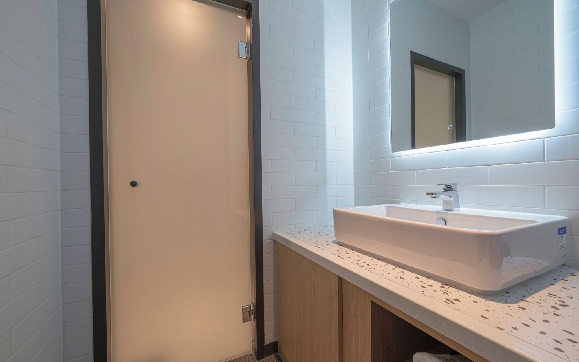 A modern bathroom with white subway tiles, a white sink with a single faucet, and a mirror above the sink.
