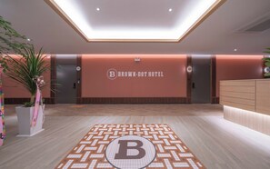 A hotel reception area with a modern design, including a reception desk, a wall with the hotel's name, and a geometric patterned floor. - Brown Dot Geobuksum (Siheung)