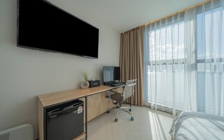 Habitación de hotel con televisor de pantalla plana, escritorio con computadora, silla, refrigerador pequeño y cama.