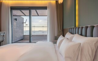 A hotel room with a large bed, a view of the sea, and a sliding glass door leading to an outdoor area.