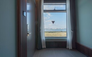 A room with a window overlooking a cityscape, a door with a handle, and a radiator below the window.