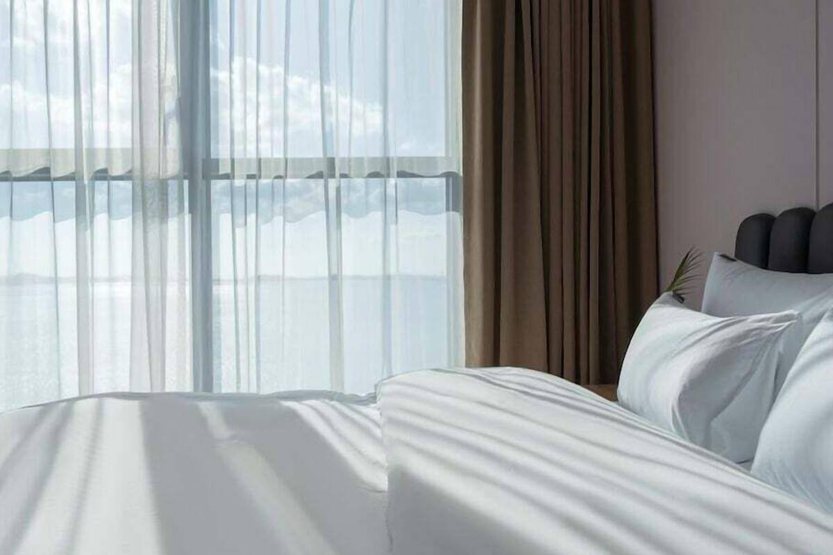 A hotel room with a large bed, sheer curtains, and a view of the sky.