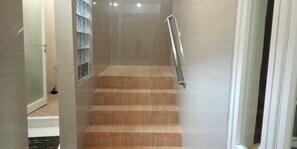 A staircase with wooden steps and a metal handrail, leading to a room with a tiled floor and a door. - BLOOMINGTON (Surabaya)