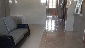 A room with a grey sofa, a tiled floor, and a glass door leading to another area. - BLOOMINGTON (Surabaya)