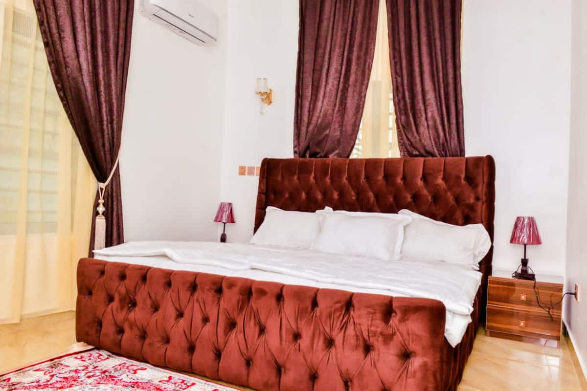 A bedroom with a large bed, two bedside tables, a wall-mounted air conditioner, and a patterned rug.