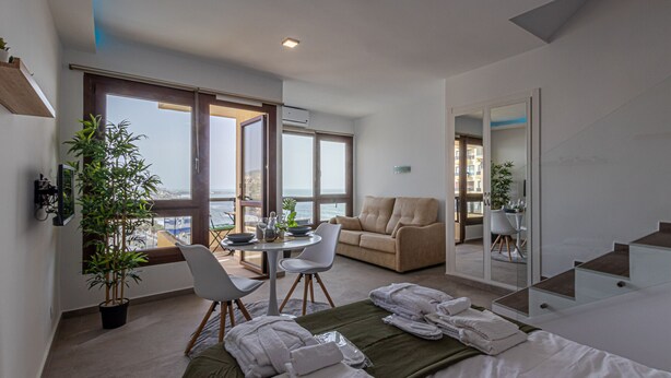 Una habitación de hotel moderna con balcón, zona de comedor, sofá y cama.