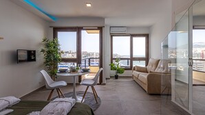 Una sala de estar moderna con sofá, mesa de comedor con sillas, televisor y balcón con vistas a la ciudad.