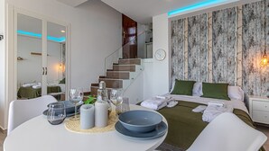 Habitación de hotel moderna con una mesa redonda, una cama con almohadas verdes, una escalera de madera y una pared con papel tapiz texturizado.