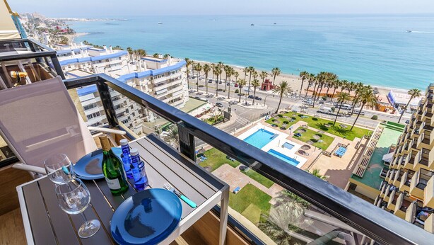 Ein Balkon mit Tisch für zwei Personen, mit Blick auf einen Ferienort, der einen Pool, Palmen und Meerblick bietet.