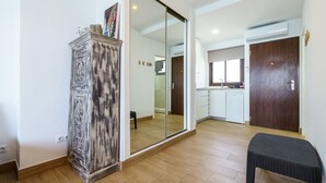 Ein geräumiges Zimmer mit großem Kleiderschrank, einer Schiebetür zu einem Badezimmer und einer Küchenzeile mit weißen Schränken und einem Fenster.