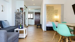 Ein modernes Wohnzimmer mit einem grauen Sofa, einem weißen Beistelltisch mit Weinflaschen und einem Essbereich mit türkisfarbenen Stühlen und einem Holztisch.