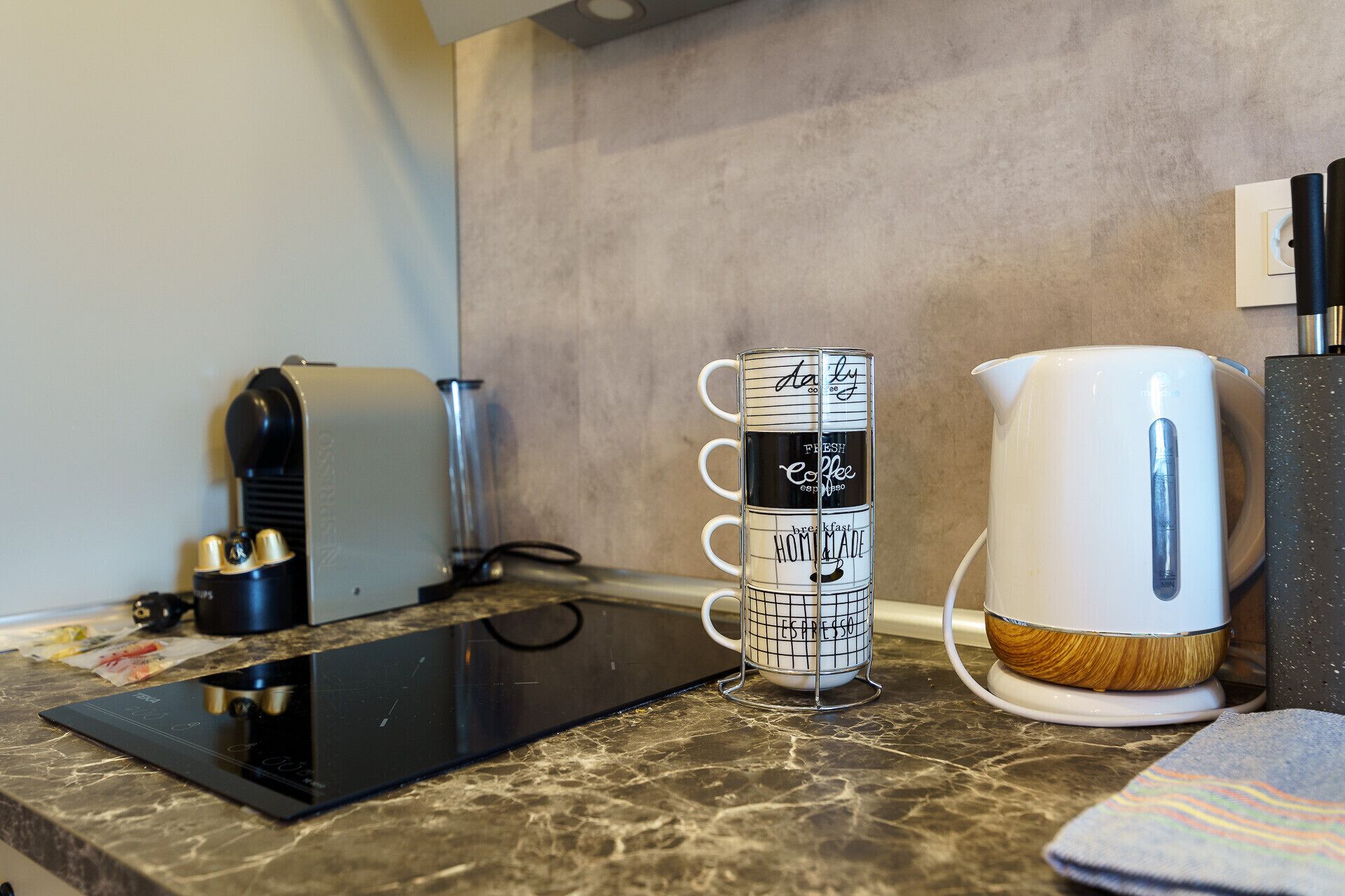 A kitchen counter with a coffee maker, a kettle, and a mug with a grid pattern.