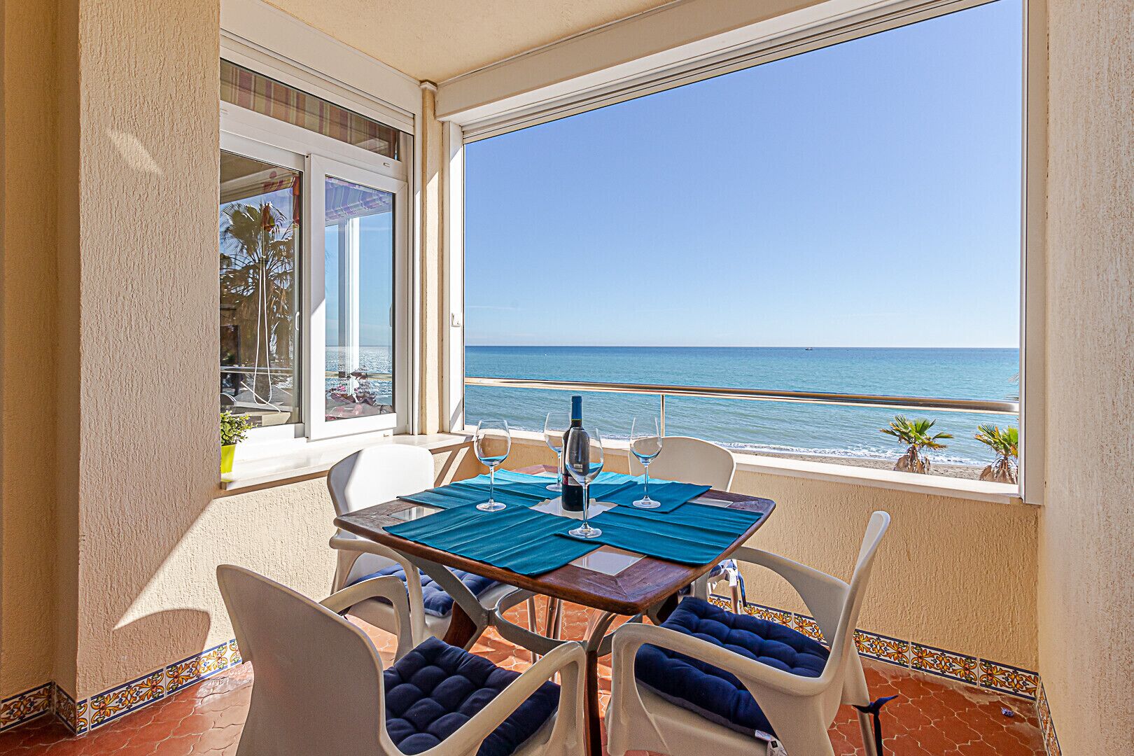 A balcony with a table set for two, overlooking a beach.