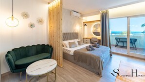 A modern bedroom with a bed, a green sofa, a small round table, and a balcony with a view of the sea. - Seaview beachfront studio with aqua park & balcony REF007 (Benalmádena)