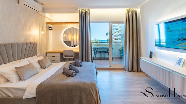 A modern hotel room with a large bed, a desk with a chair, a round mirror, and a TV mounted on the wall. - Seaview beachfront studio with aqua park & balcony REF007 (Benalmádena)