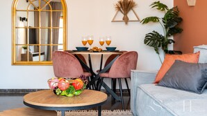 Un comedor con una mesa redonda, dos sillas rosas y un frutero sobre una mesita.