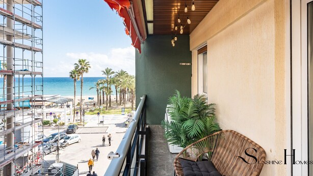 Un balcón con vista a la playa, una silla de mimbre y una planta en maceta.