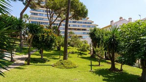 Un jardin bien entretenu, agrémenté de divers arbres et arbustes, avec un chemin dégagé et un immeuble à plusieurs étages en arrière-plan.