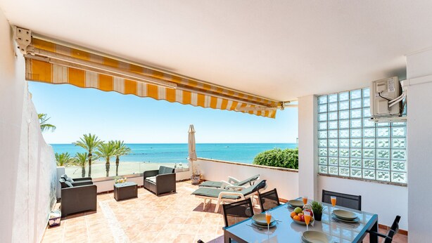 Un espace extérieur abrité, avec une table dressée pour les repas, des chaises longues et une vue sur la mer.