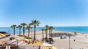 Une plage bordée de palmiers, une rangée de parasols et une rangée de bateaux.