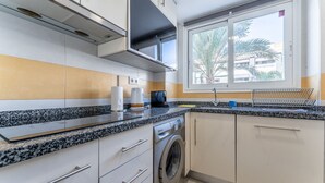 Eine kompakte Küche mit Waschmaschine, Mikrowelle und Fenster mit Blick auf Palmen.