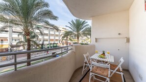 Ein Balkon mit Tisch und Stühlen mit Blick auf eine Straße, gesäumt von Palmen und Gebäuden.