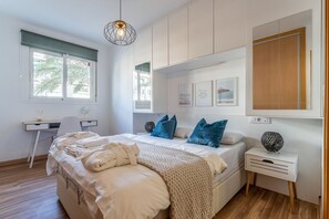 Un dormitorio con cama, mesitas de noche, un escritorio y un ventanal grande.