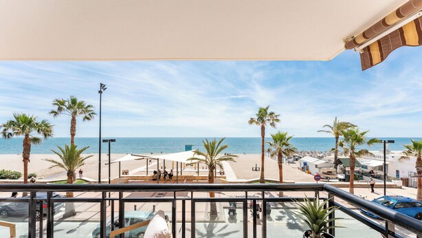 A balcony with a view of a beach, palm trees, and a clear sky. - Superb Location Beachfront , 3 bed with terrace REF044 (Fuengirola)