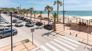A coastal road with parked cars, palm trees, a pedestrian crossing, and a beach in the background. - Superb Location Beachfront , 3 bed with terrace REF044 (Fuengirola)