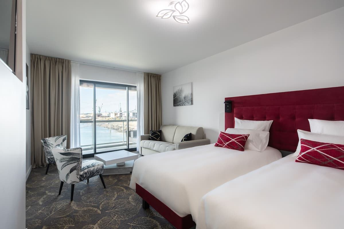 Une chambre d’hôtel avec un grand lit, un canapé, un fauteuil et une vue sur la ville par la fenêtre.