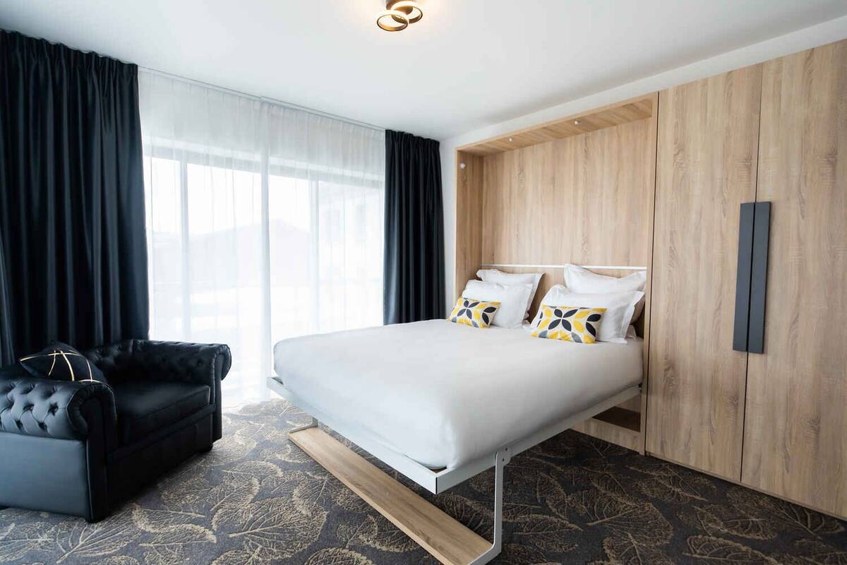 Une chambre d’hôtel moderne avec un lit, un canapé en cuir noir et une armoire en bois.