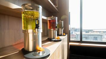 A coffee machine and a tea dispenser on a wooden counter by a window.