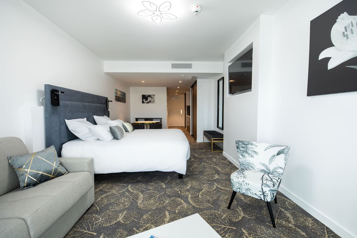 Une chambre d’hôtel moderne avec un grand lit, un canapé, un fauteuil et un bureau.