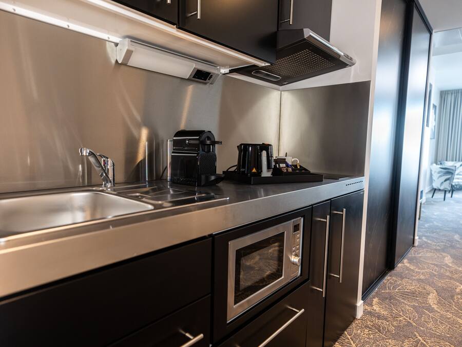 Una cocina moderna con un lavamanos de acero inoxidable, una cafetera y un microondas.