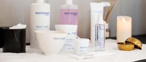 Un tocador de baño con artículos de aseo, incluyendo botellas de Phytomer, un cuenco blanco, un cuenco dorado y una vela.