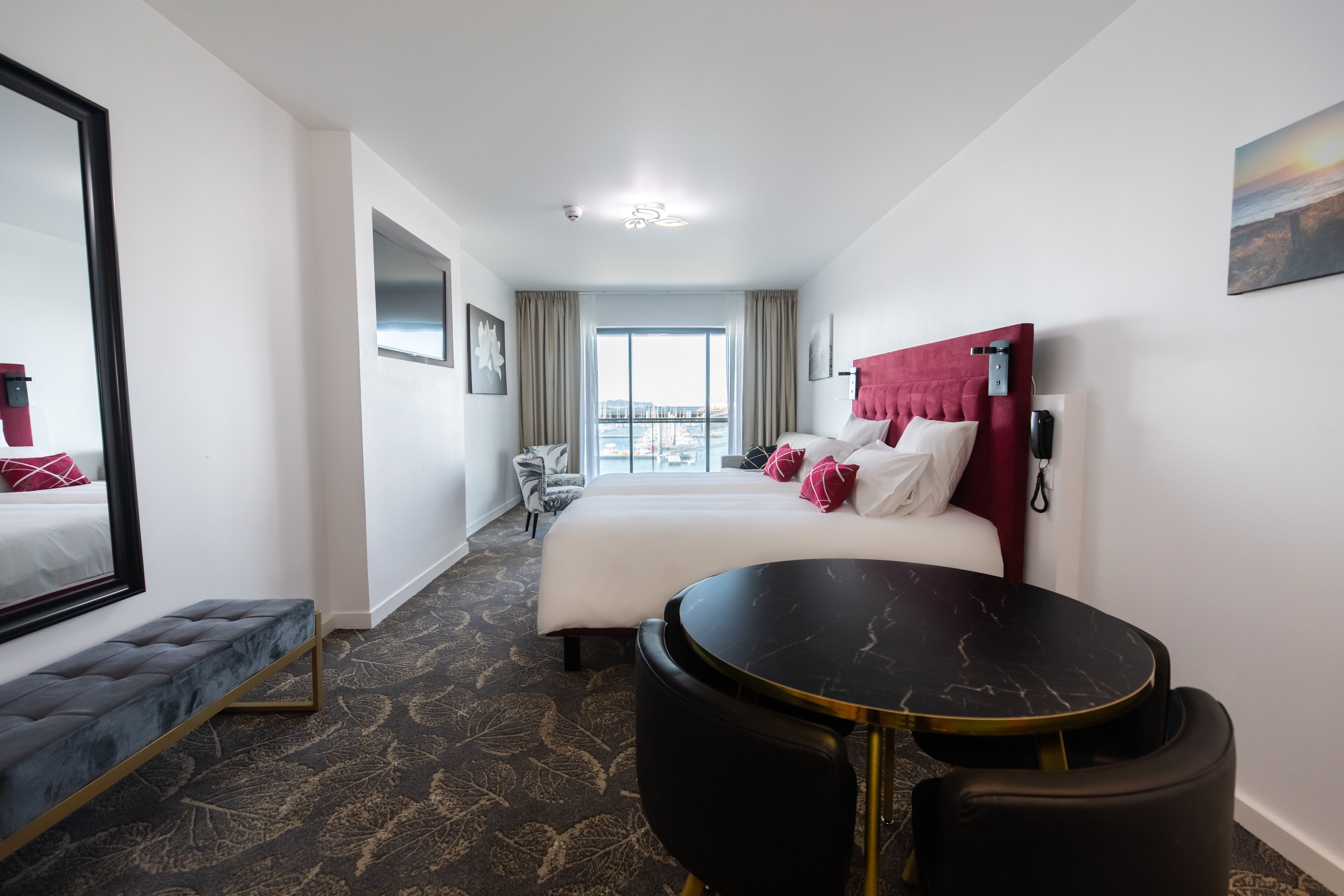 Habitación de hotel con una cama grande, un escritorio, un banco y vistas de la ciudad a través de la ventana.