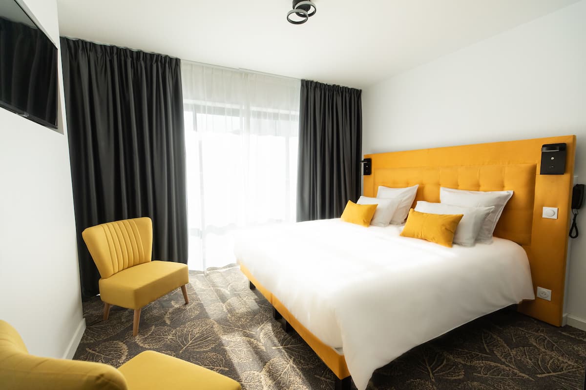 Une chambre d’hôtel avec un grand lit, un fauteuil jaune et un canapé.