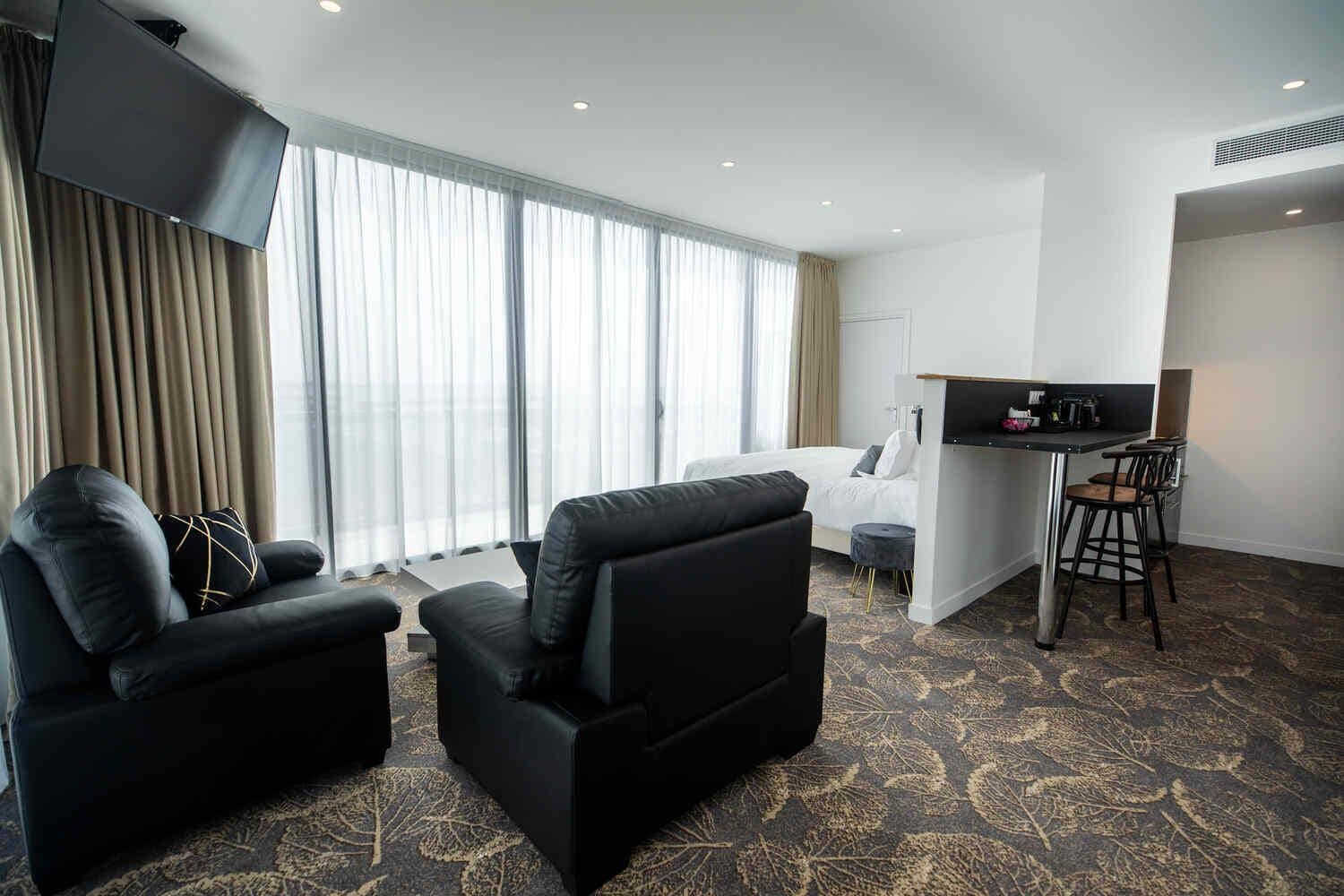 Una camera d'albergo con un letto, due poltrone nere, un tavolino e un angolo bar.