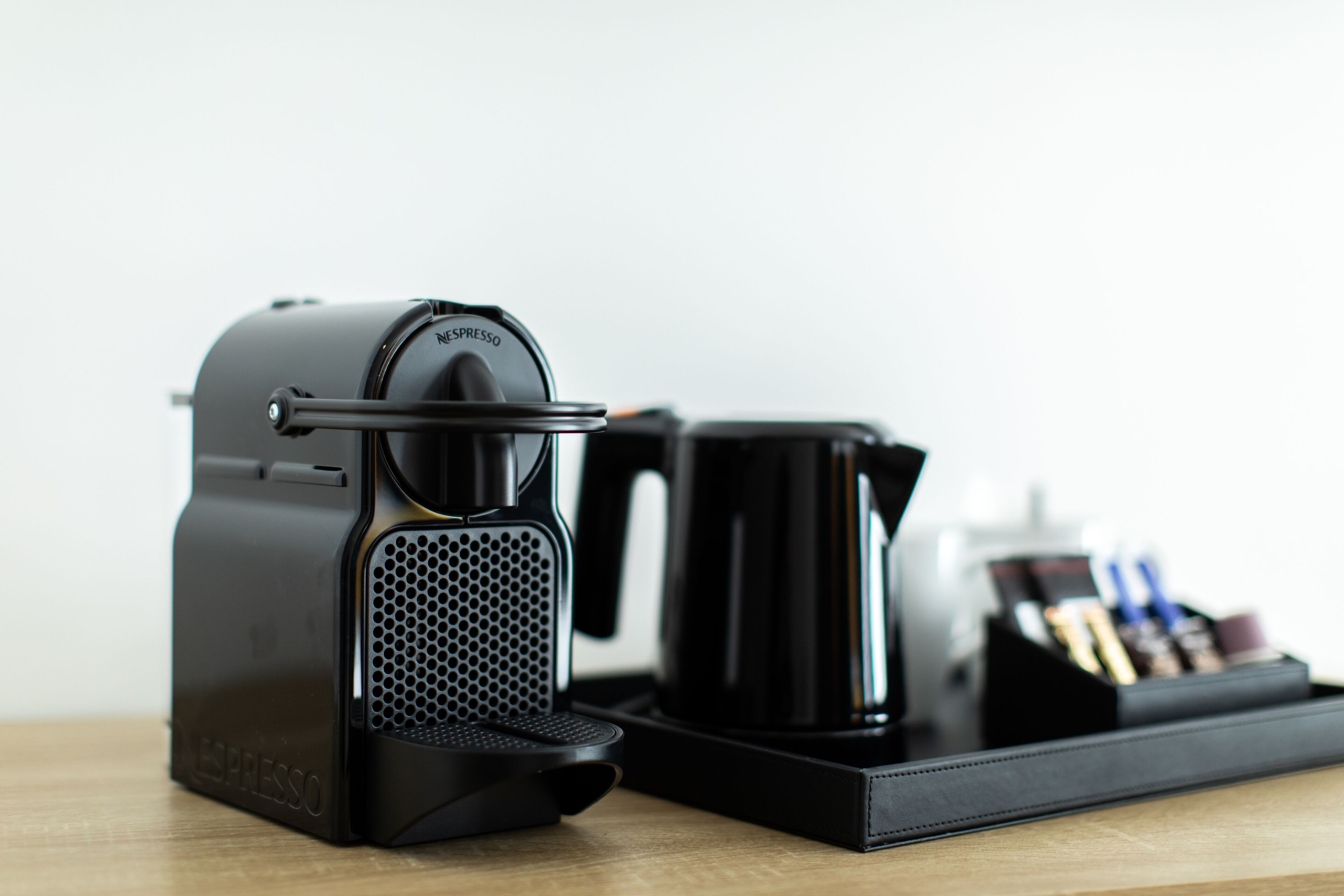 Una máquina de café Nespresso sobre una bandeja con una jarra de café negro y un juego de cápsulas de café.