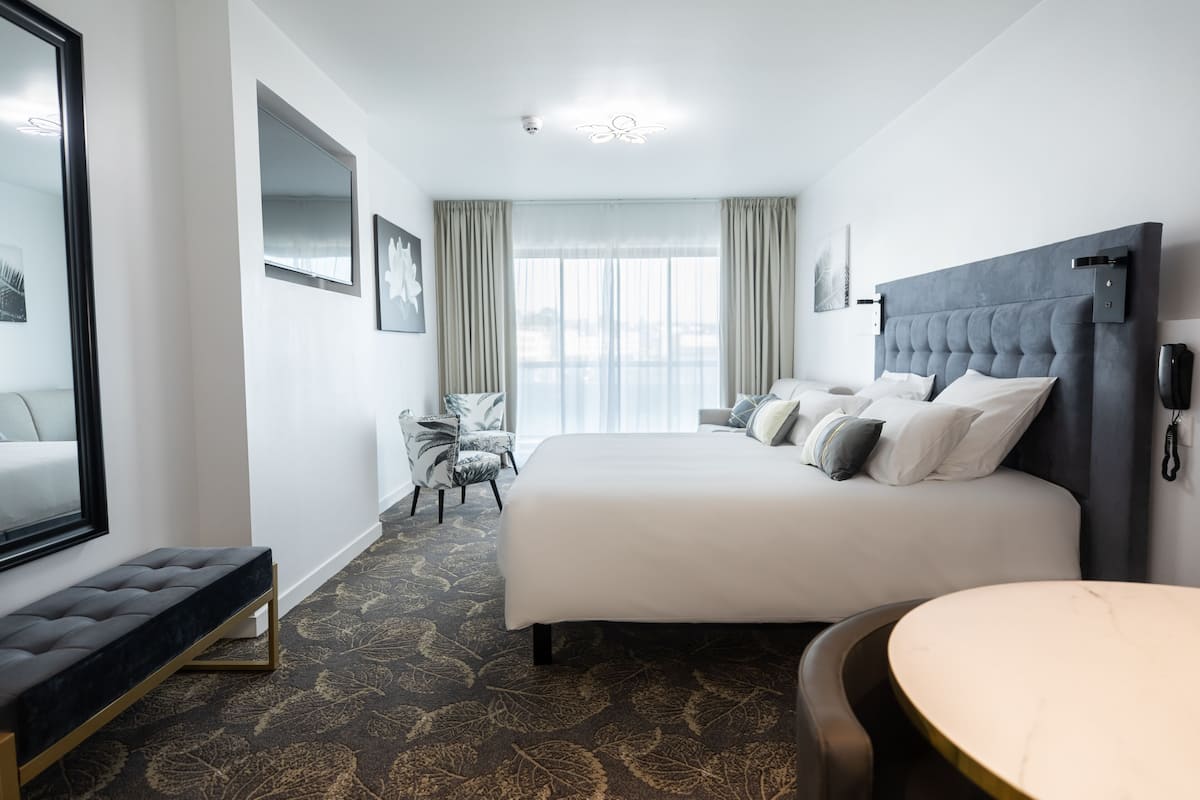 Une chambre d’hôtel moderne dotée d’un grand lit, d’une banquette, d’une table ronde et offrant une vue sur la ville grâce à de grandes fenêtres.