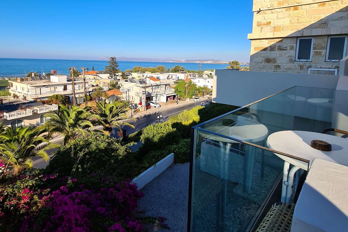 A modern building with a glass balcony overlooking a coastal town.