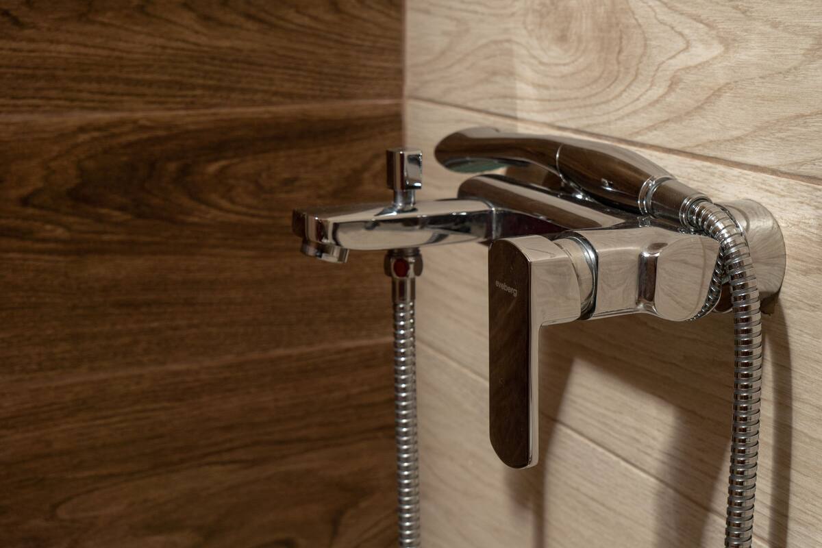 A chrome showerhead with a flexible hose attached to a wall-mounted faucet.