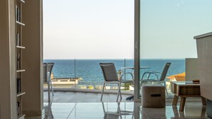 A spacious balcony with a view of the sea, a seating area with chairs, and a wooden table. - Abella Hotel (Chania)