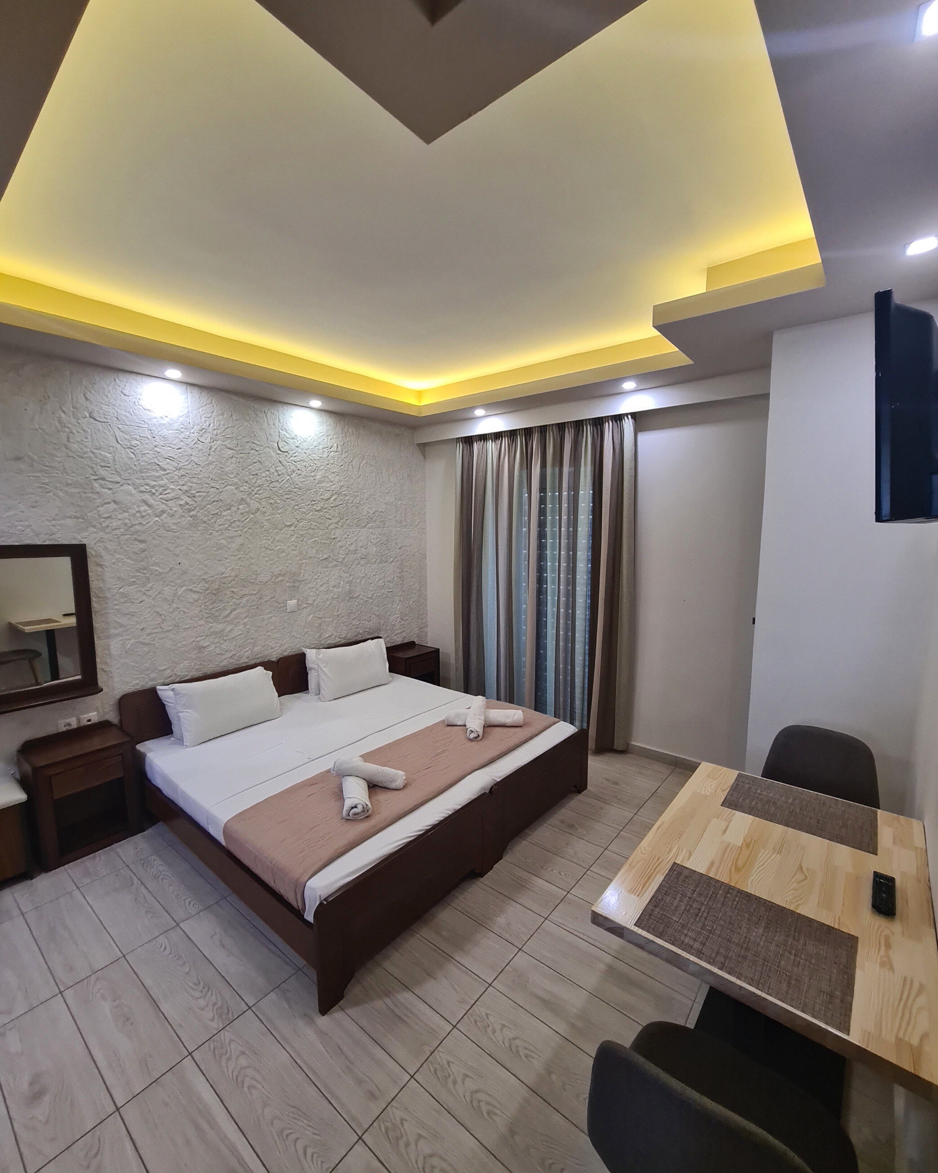 Quarto de hotel moderno com uma cama grande, mesas de cabeceira, escrivaninha e vista para a cidade através da janela.