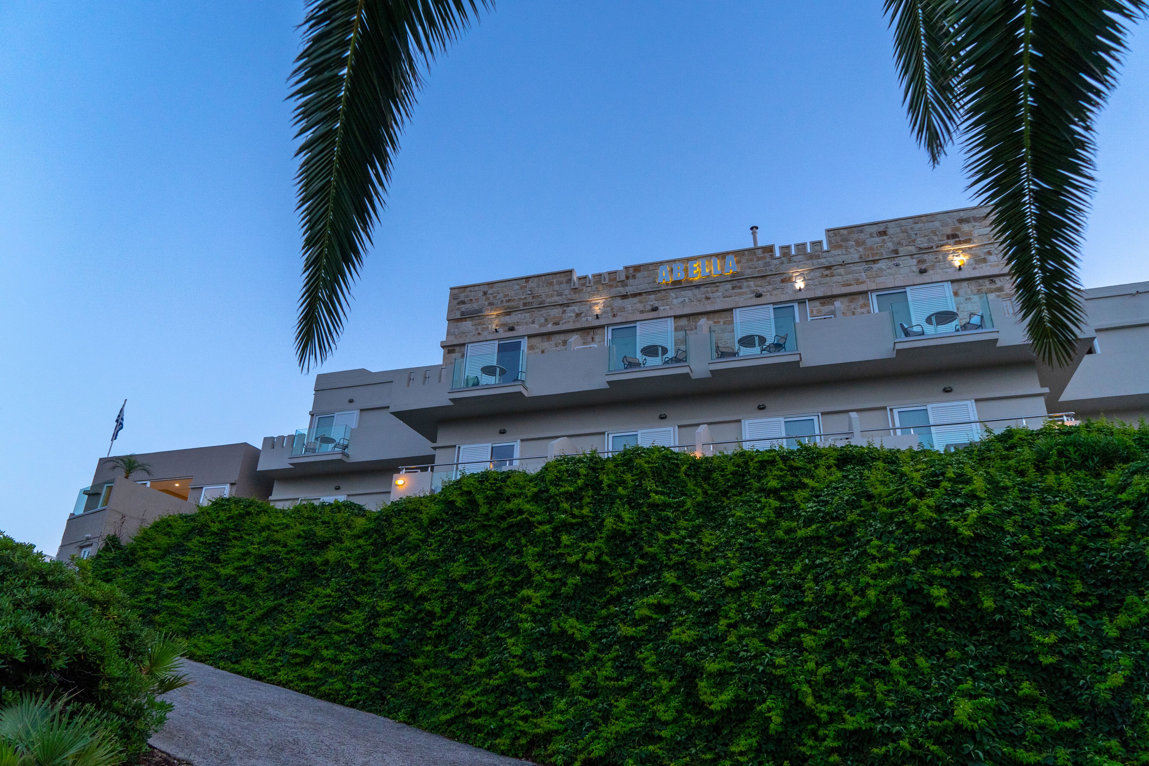A multi-story hotel with balconies, a landscaped hill, and a clear sky.
